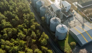Vista aérea de silos metálicos industriais ao lado de uma estrada e floresta verde, que ilustram empresas de biogás em artigo da Apema.